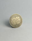 Bronze-finished coin showing YES, standing on a light gray background