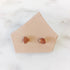 Pair of small orange gemstone stud earrings on a pale card over white marble