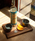Walnut board with two black copitas, orange slices and salt beside a bottle in sunlight