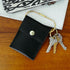 Black leather snap wallet on a brass key ring with keys on a wood table