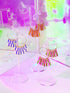 Kaleid fringe hoops in periwinkle and cream and in orange and red on clear stands under pink light